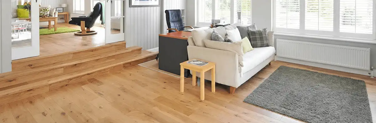 A modern living room with professionally installed laminate flooring, a beige sofa, a small side table, a gray rug, and large windows with white shutters in New Haven, CT